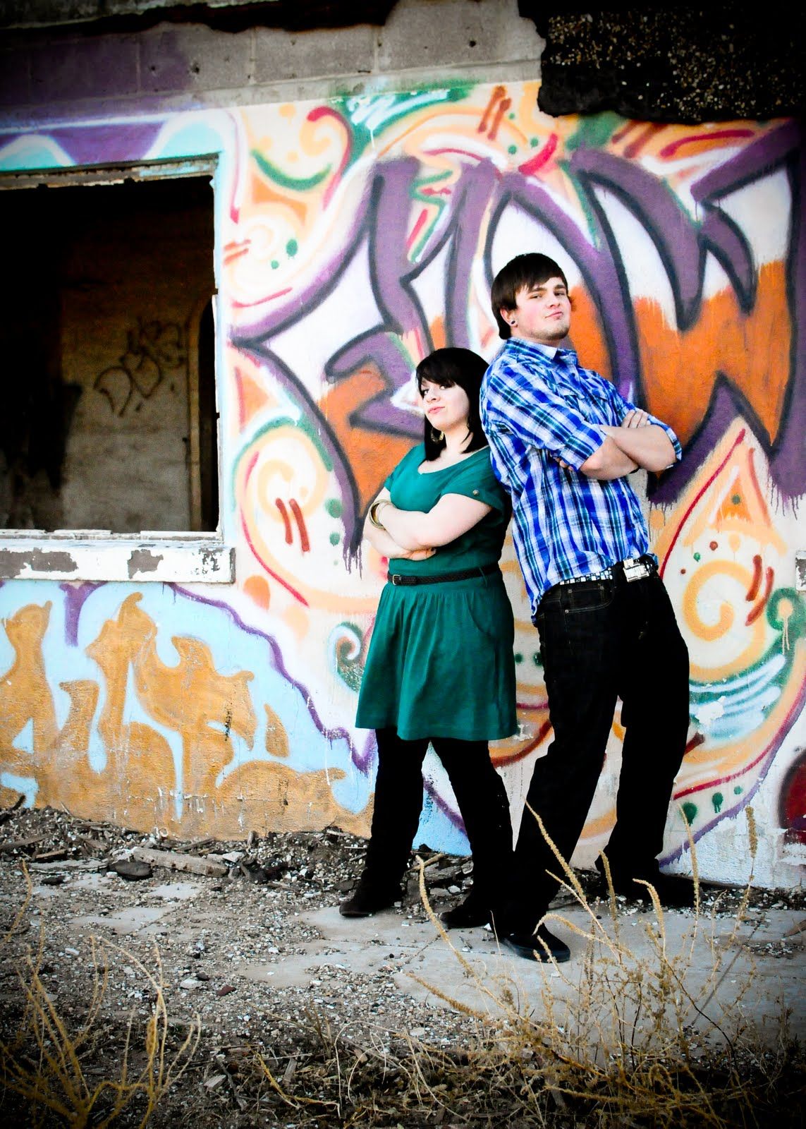 A couple poses playfully against a wall covered in vibrant graffiti art during an outdoor photo session.