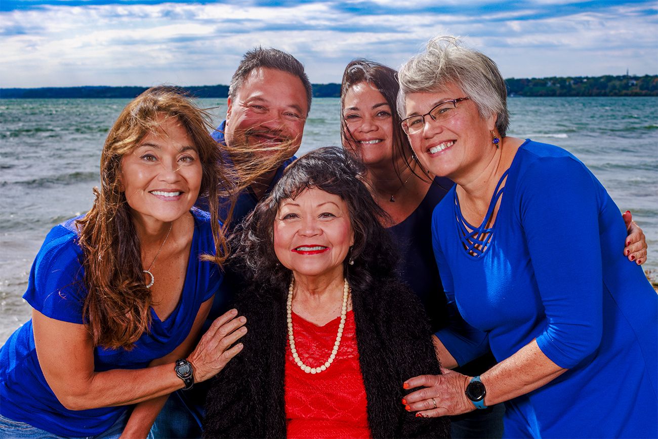 A group wearing blue and red smiles together at the beach with a waterfront backdrop on a sunny day.