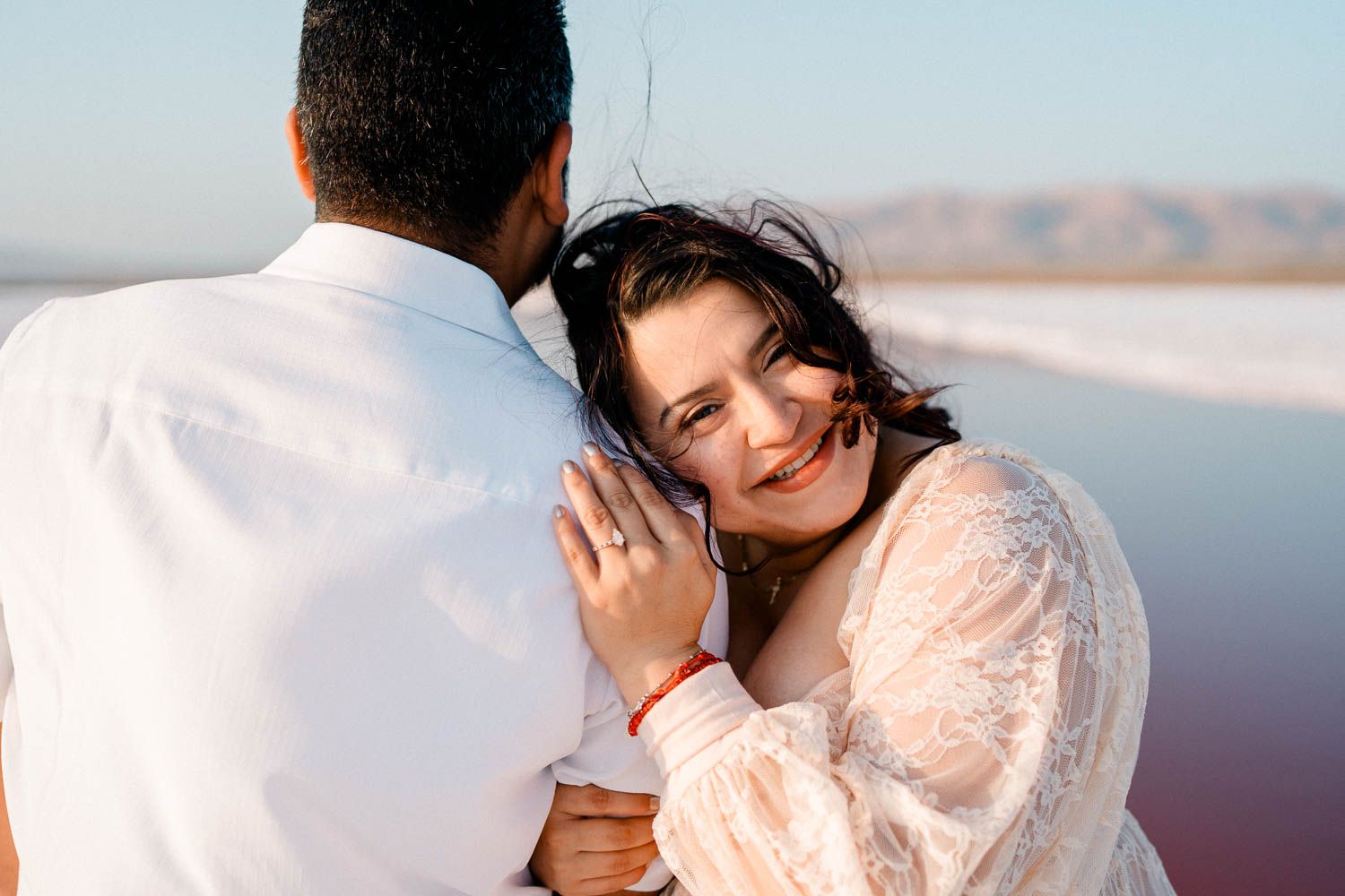 Couple in elegant wedding attire embrace during golden hour photoshoot at scenic mountain overlook.
