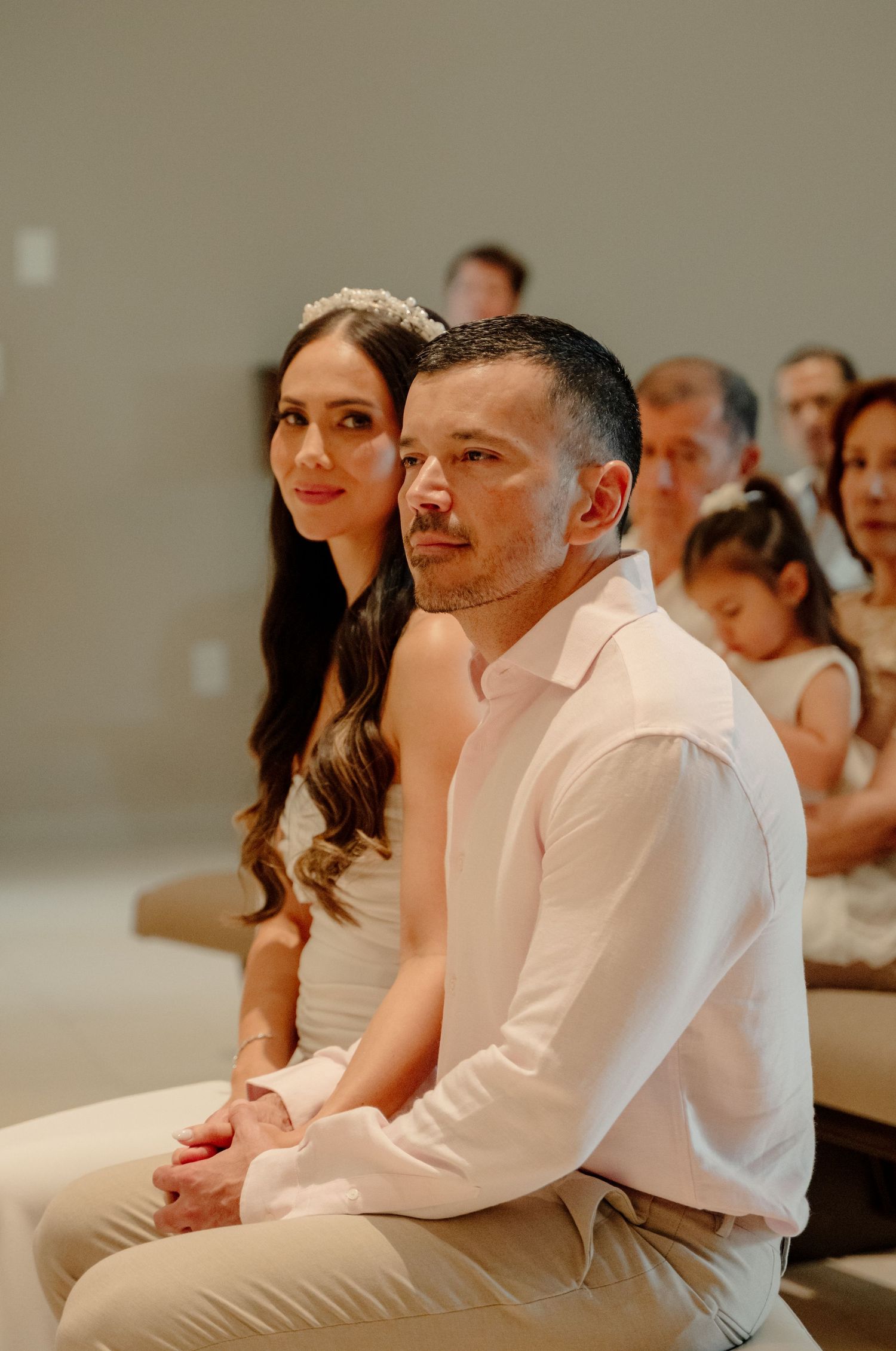 Couple sits together during a special occasion, wearing white and light-colored formal attire.