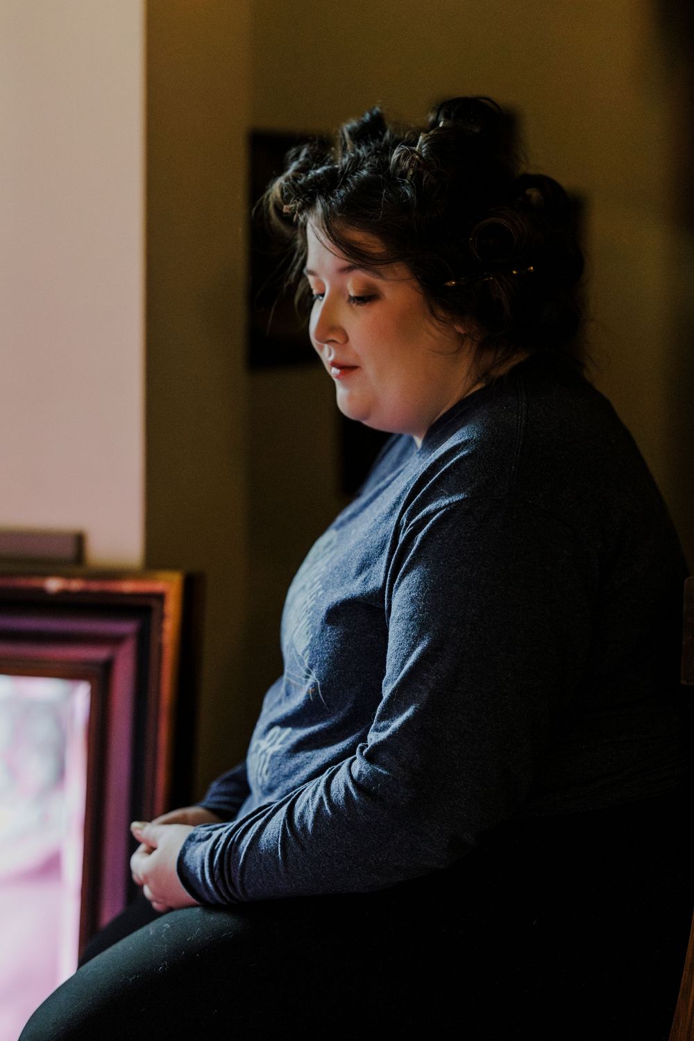 A quiet moment captured in moody lighting shows a contemplative person in a dark sweater looking downward.