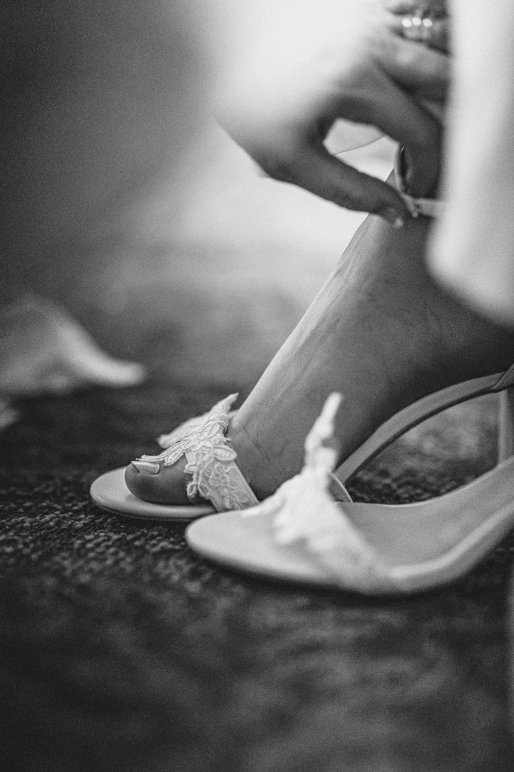 A black and white photo of lace wedding shoes being put on before the ceremony.