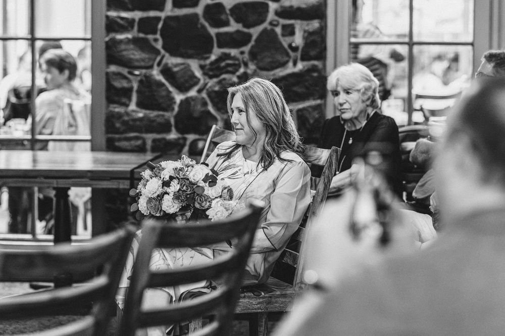 Wedding guests seated in wooden chairs watching the ceremony in a stone-walled venue.