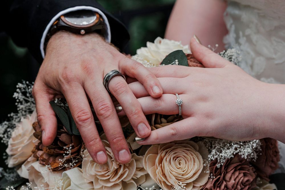 Close-up of hands exchanging rings during a wedding ceremony with soft pink roses in view.