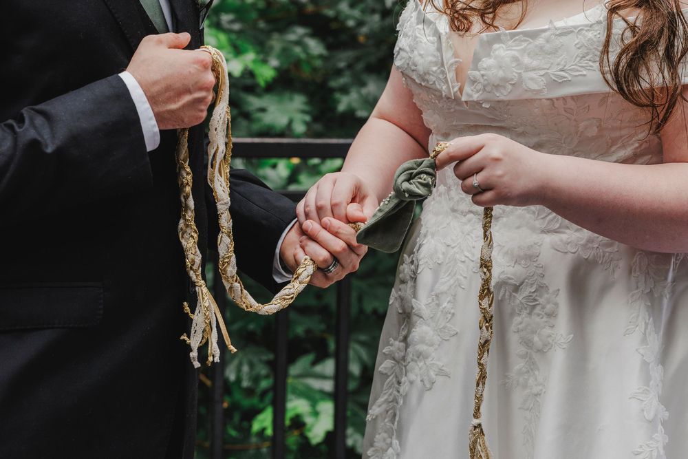 Close up of hands holding braided cord during wedding ceremony ritual.