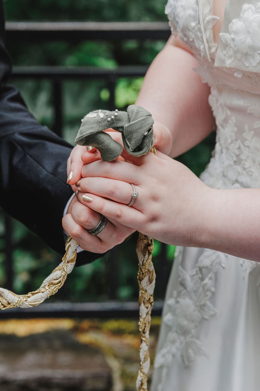 Close-up of hands holding braided rope during a traditional wedding ceremony with white lace dress detail.