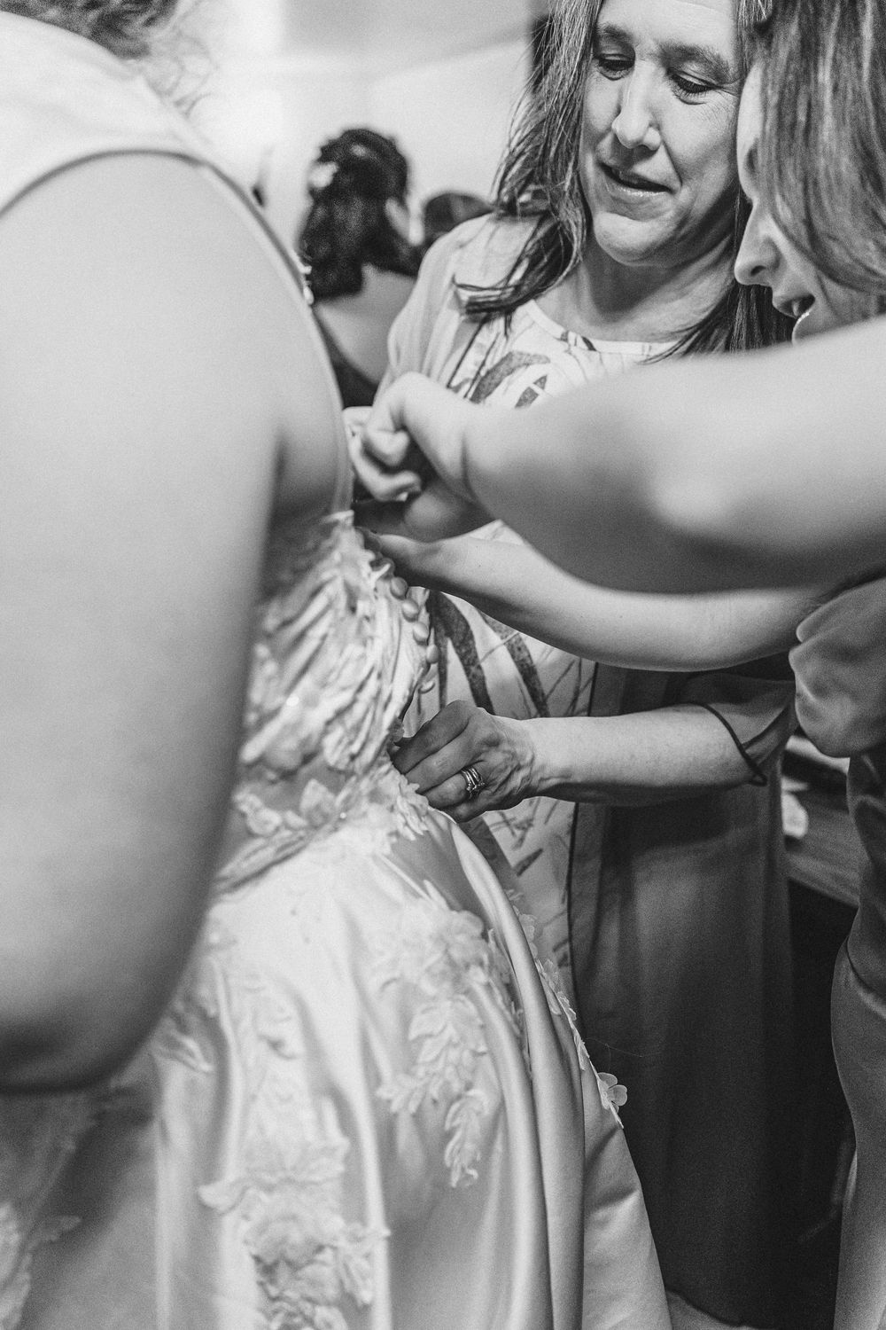 A close-up black and white photo of wedding dress details being adjusted.