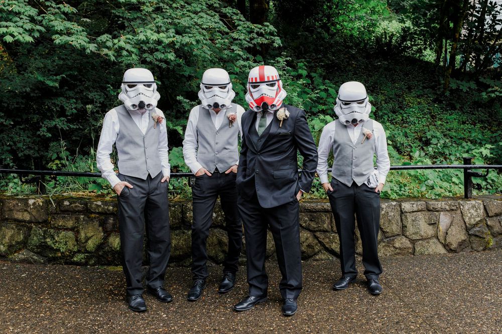 Wedding party wearing Star Wars stormtrooper masks pose against green forest background.