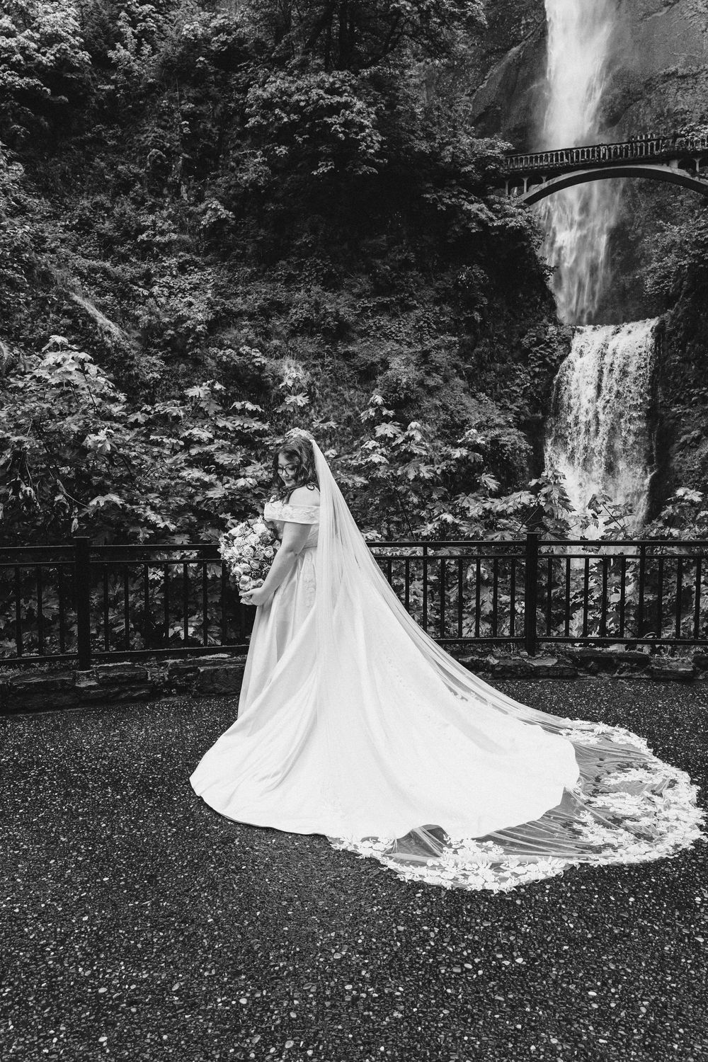 A dramatic black and white bridal portrait at Multnomah Falls with flowing veil and train.