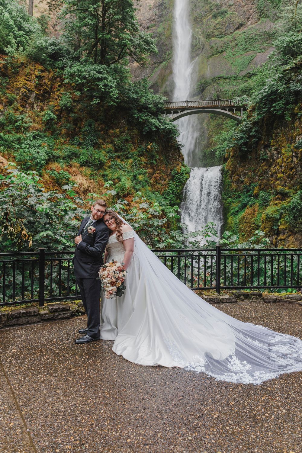 A wedding couple poses in front of Multnomah Falls with a flowing white dress train on display.