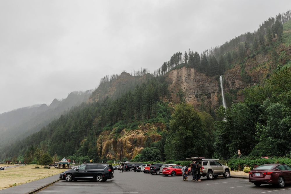 Panoramic view of misty mountain landscape with parked cars along scenic roadway.