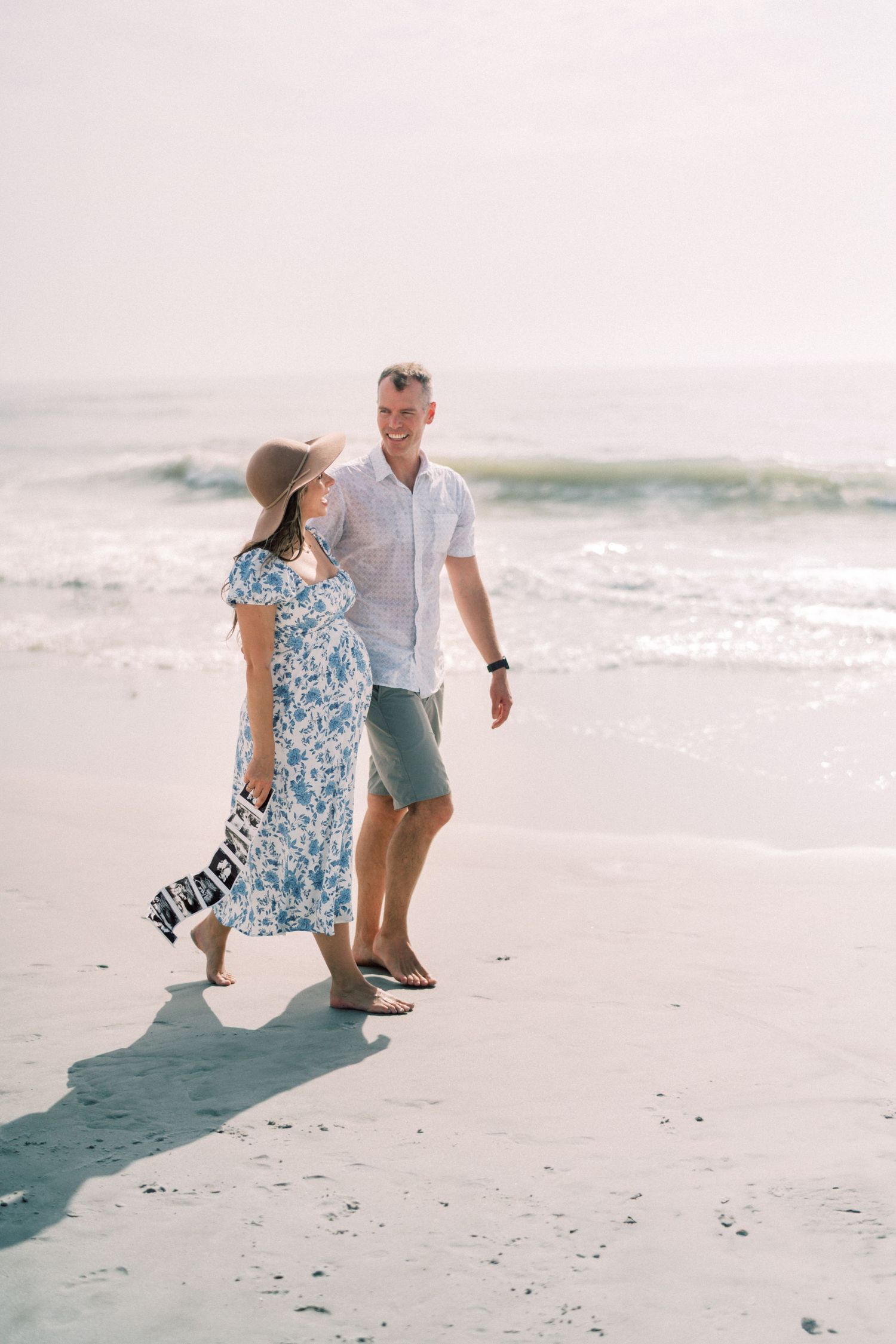 A couple strolls together on a serene beach with gentle waves and misty atmosphere creating a peaceful coastal scene.