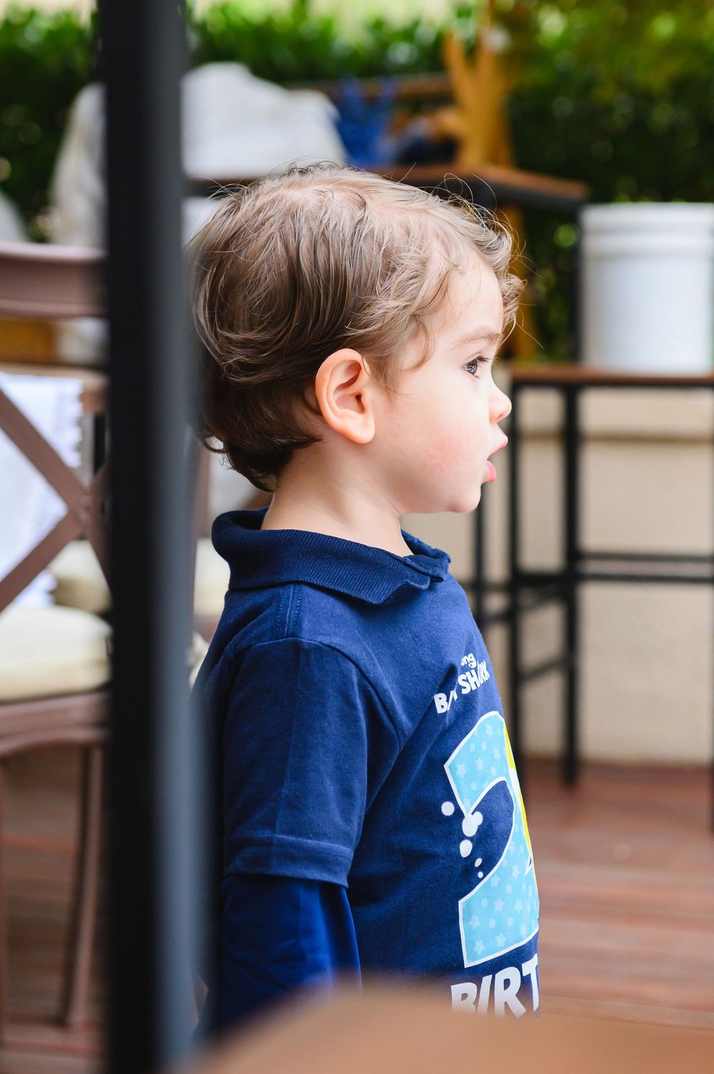 Child in navy blue polo shirt looks to the side while seated outdoors.