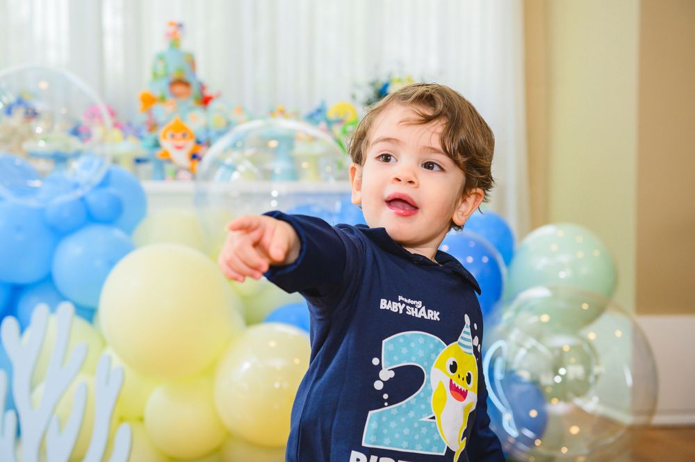 A child in a navy blue shirt plays and laughs while surrounded by colorful birthday party balloons.