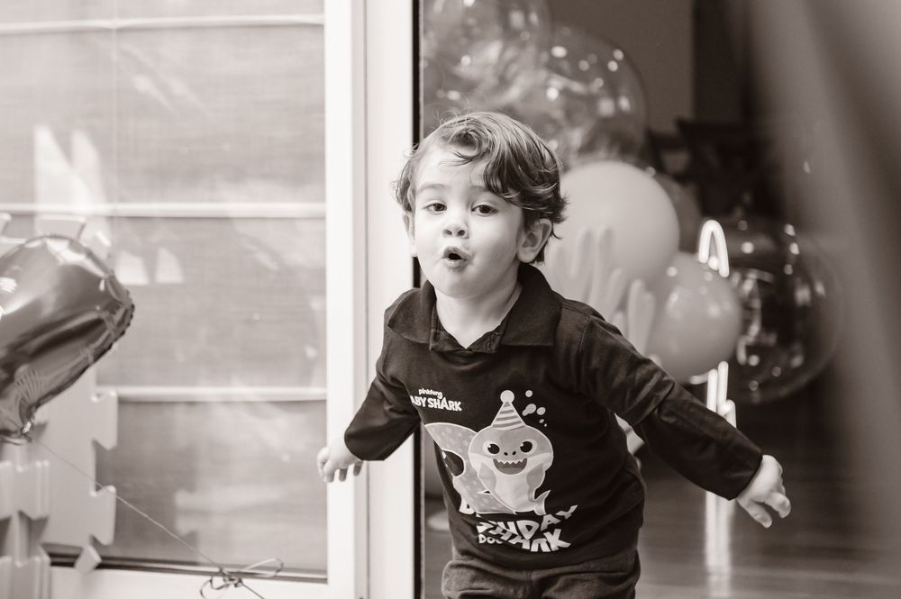 Black and white image of a joyful child in a sweater blowing bubbles during a party celebration.