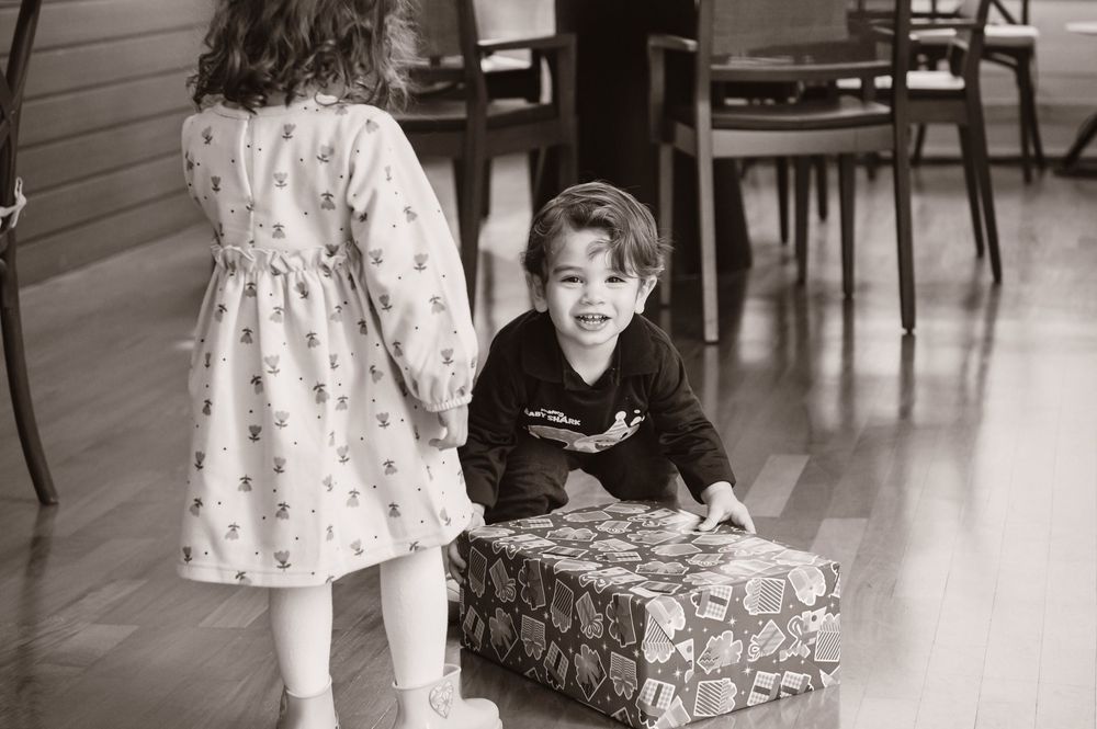A toddler holds onto a walker toy and looks joyfully towards something off camera in a brightly lit indoor space.