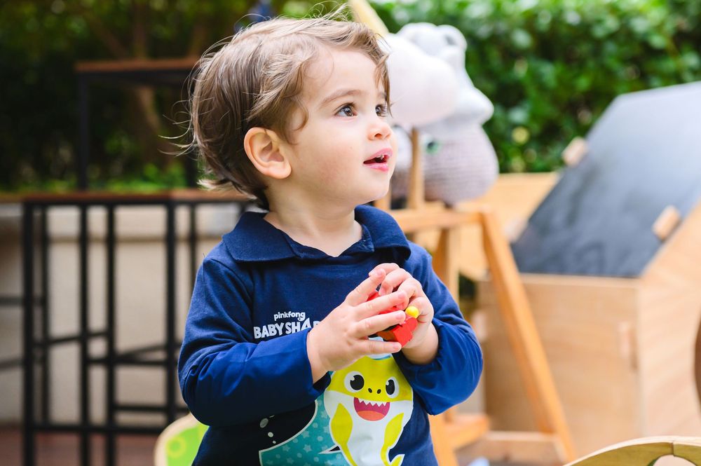 Child in a navy sweater holding colorful stacking toys while playing at a table on an outdoor patio.
