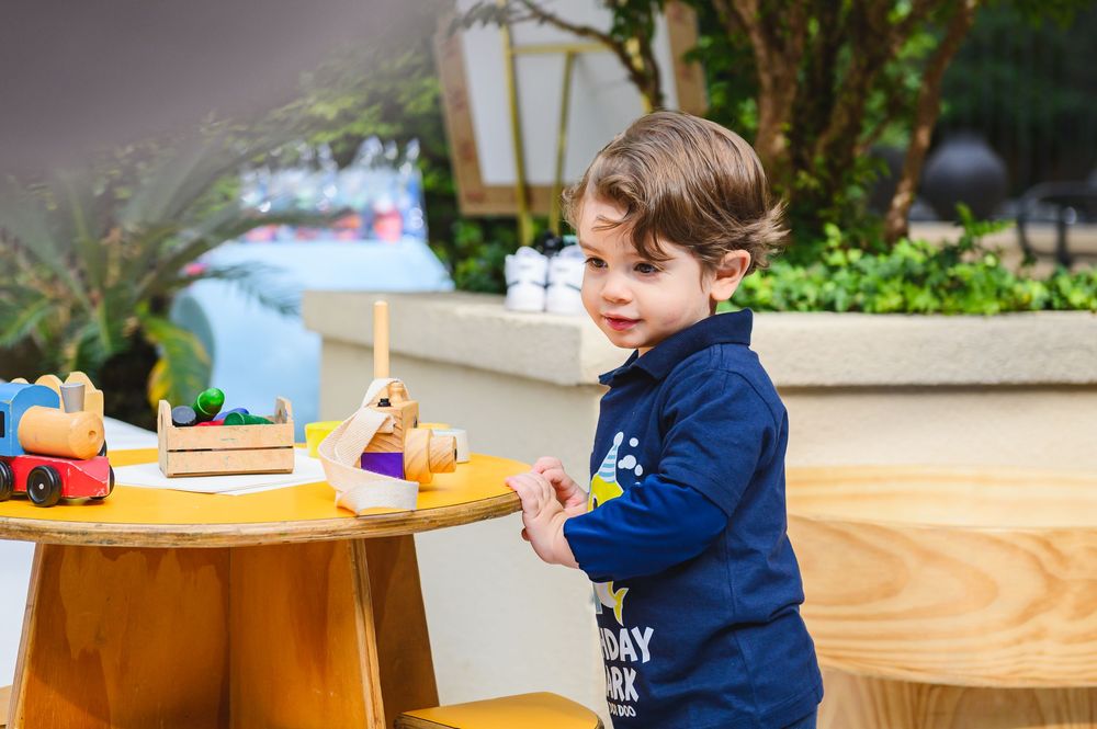 Child in navy blue sweater playing at yellow activity table with toys during playtime.