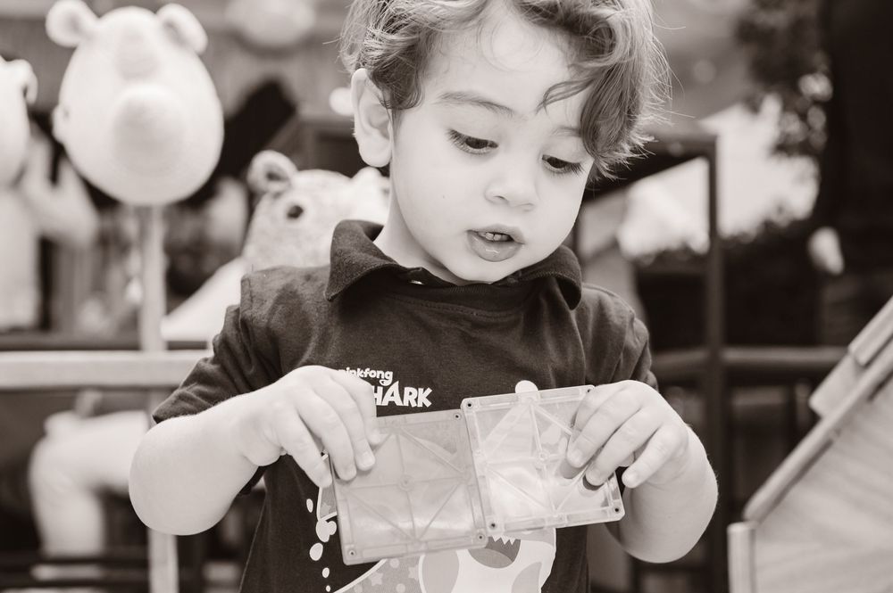 A small child in black and white photograph examining a toy or object with intense concentration and curiosity.