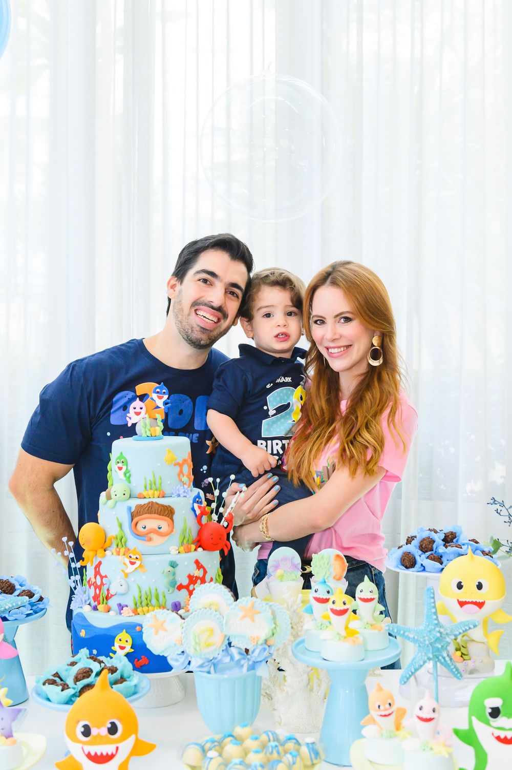 A colorful Baby Shark themed birthday party dessert table features a multi-tiered cake and decorated cupcakes.