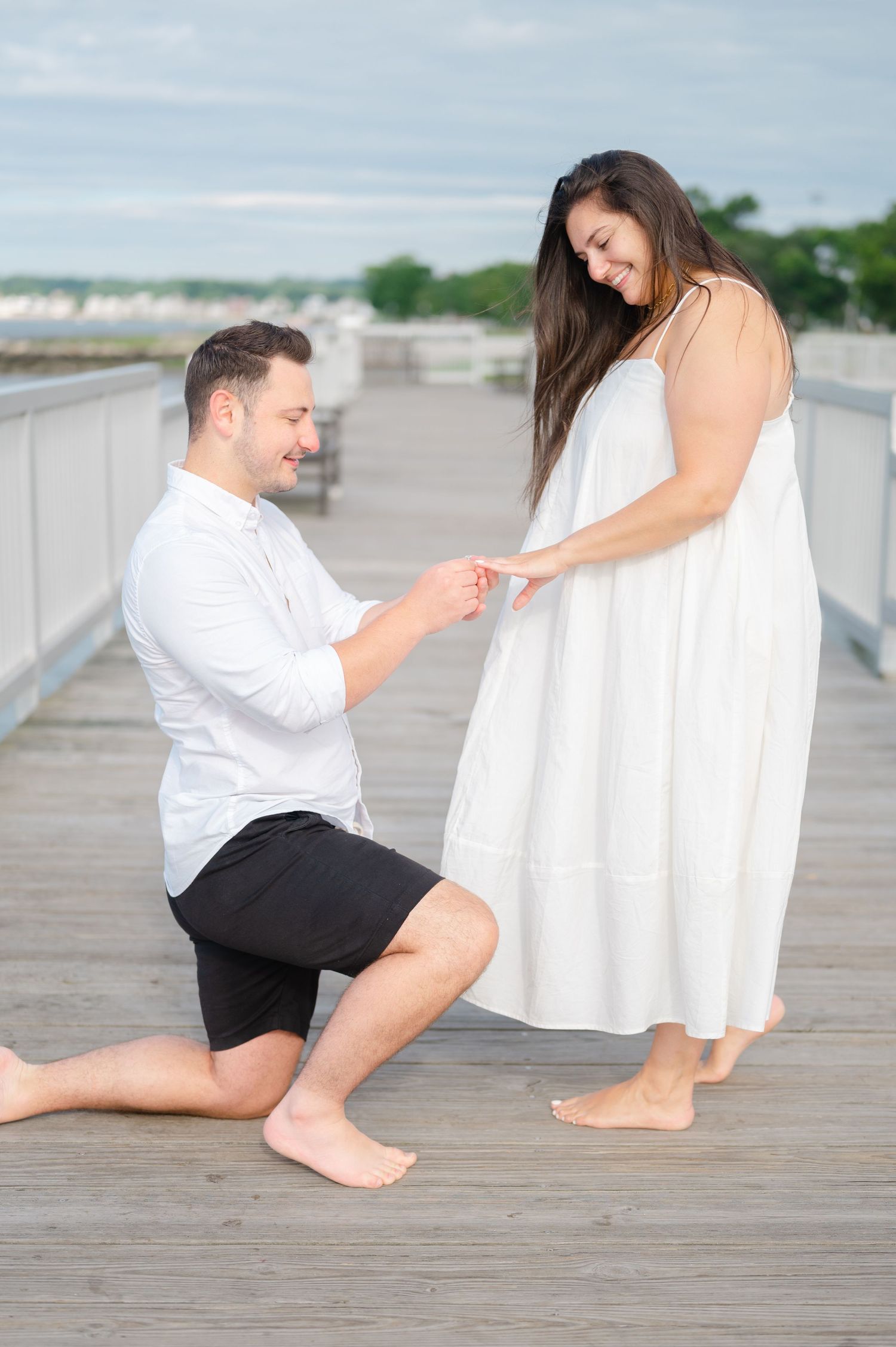 A romantic couple gets engaged on a pier in Fairfield County, CT. The man slips a ring on the woman's finger.