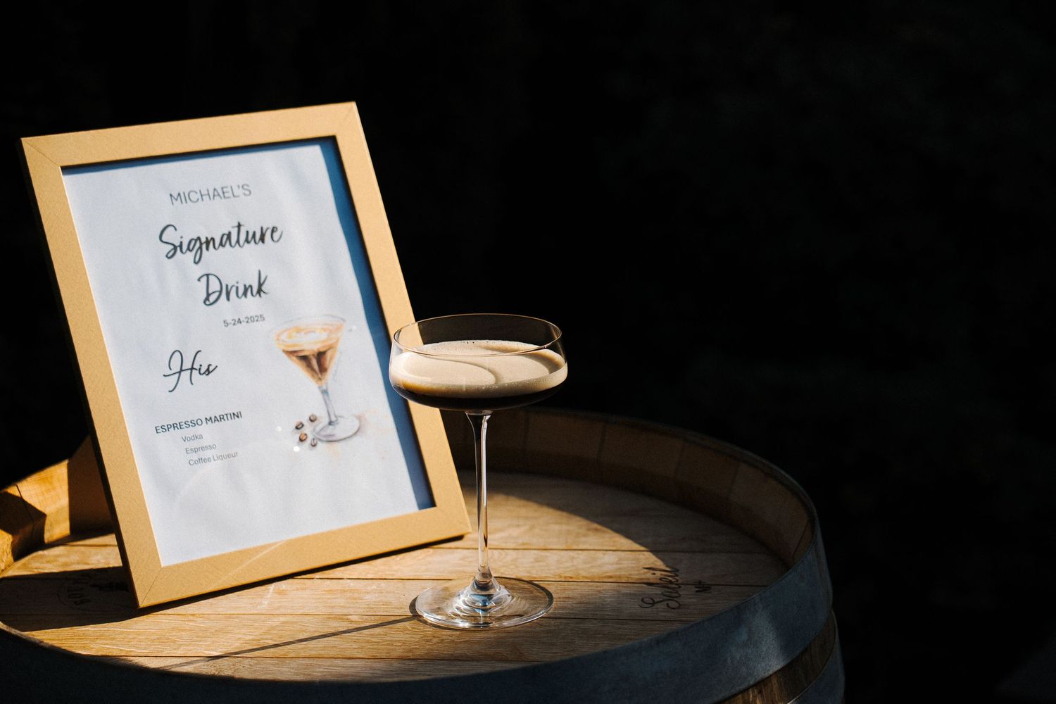 A wooden frame displays a 'Signature Drink' menu card beside an elegant cocktail glass on a dark round table.