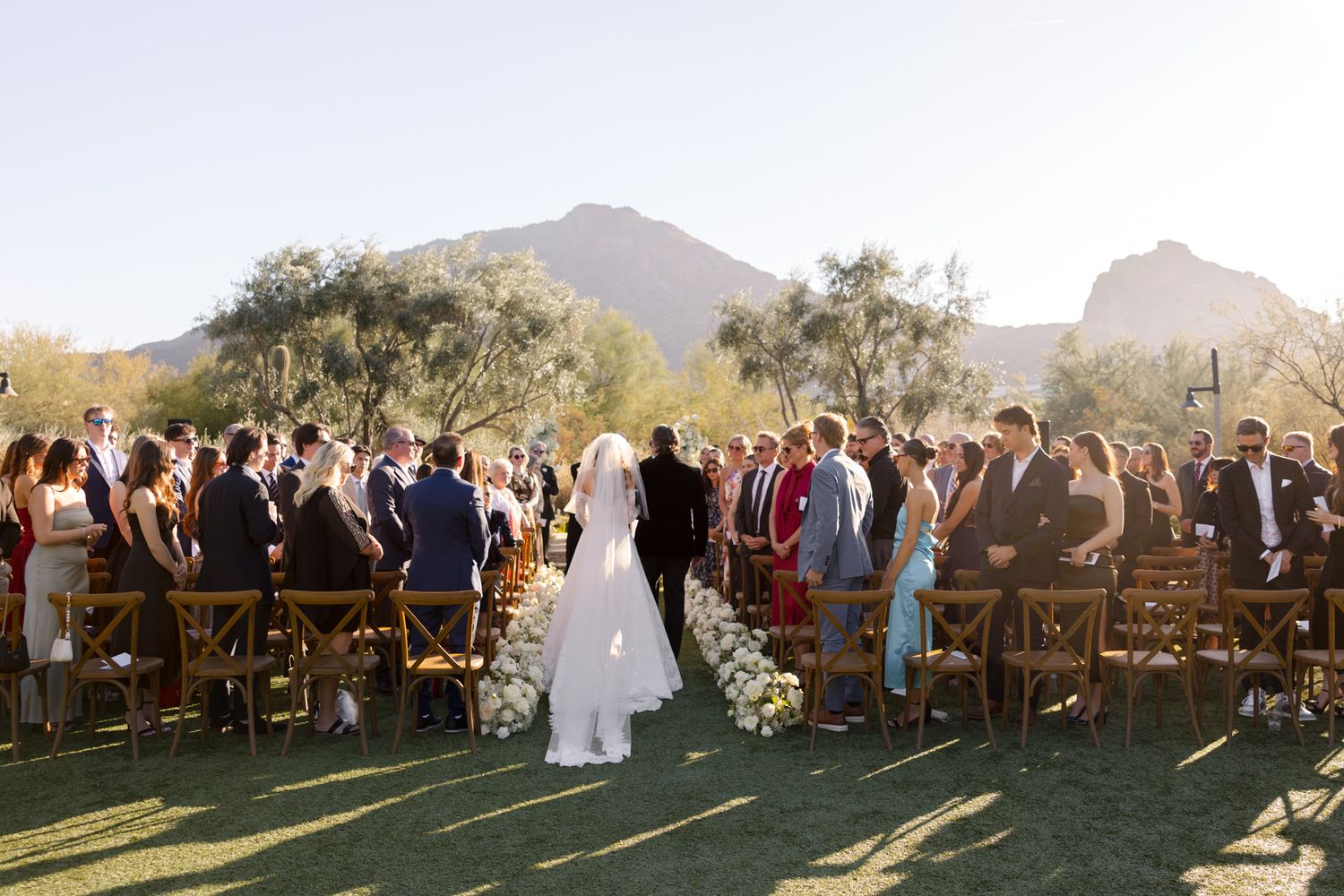 Outdoor wedding ceremony in scenic desert landscape with mountain backdrop and wooden chairs for guests.