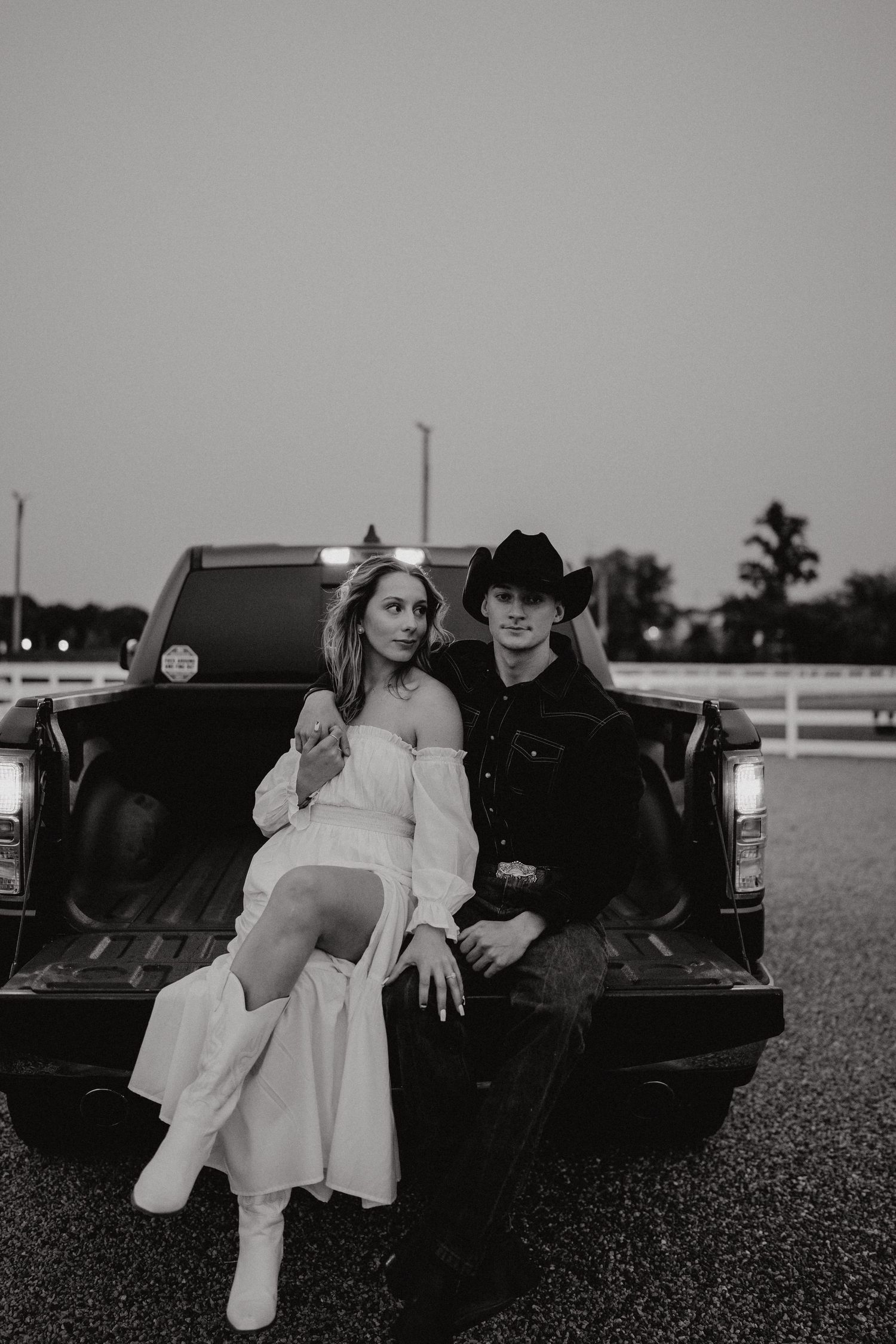 Black and white photo of a couple sitting on a pickup truck tailgate in country setting.