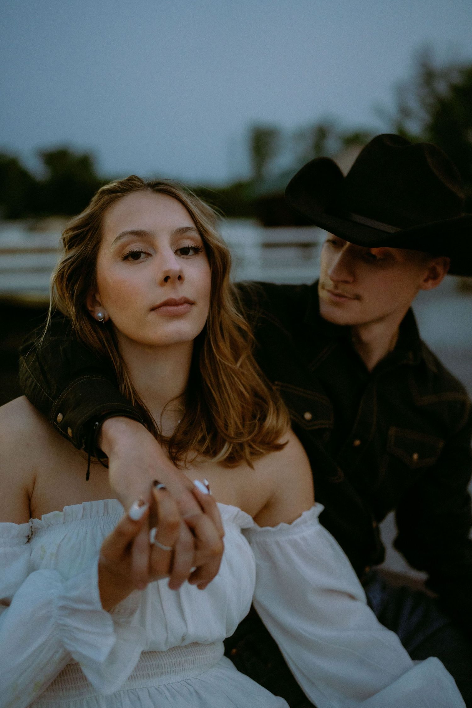 A romantic couple in western-inspired outfits share an intimate moment at dusk.