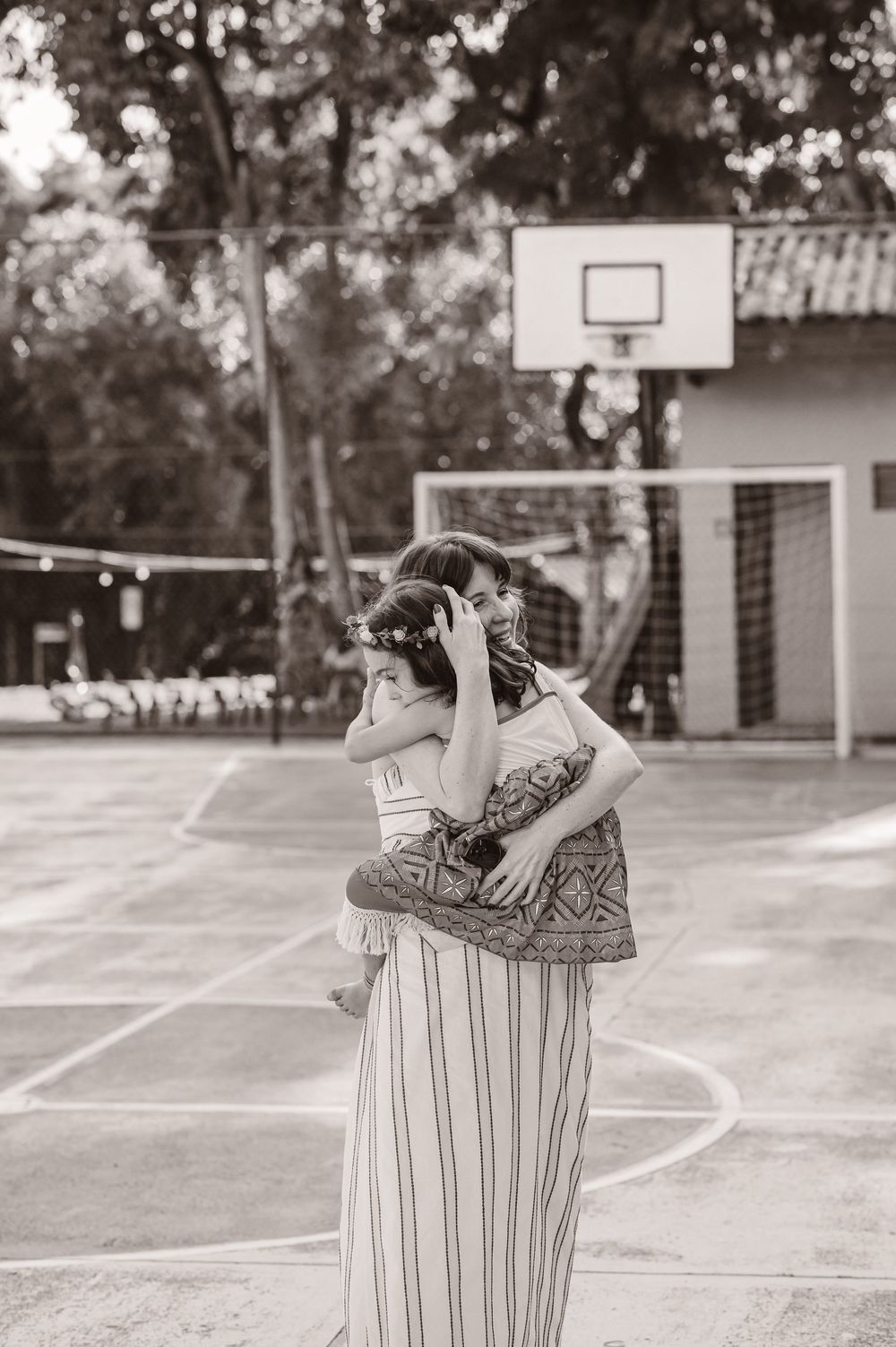 A black and white photo of a parent and child embracing on a basketball court with a hoop in the background.
