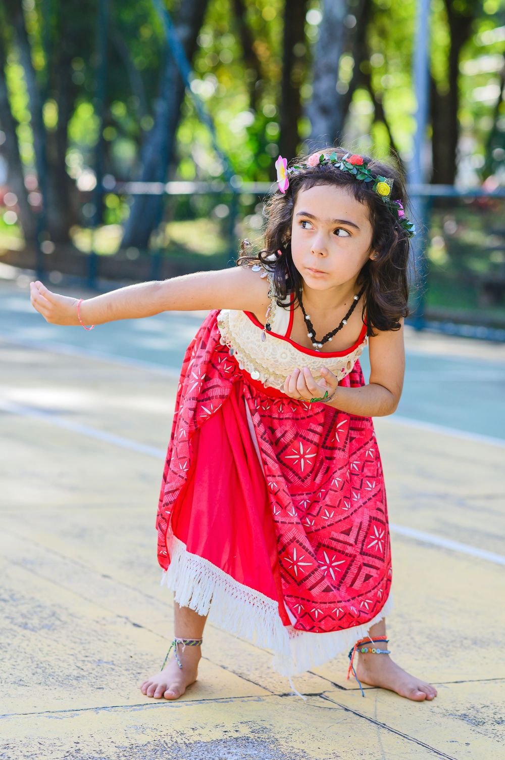 Young child in bright red dress strikes playful poses outdoors in a park setting on stone pavement.