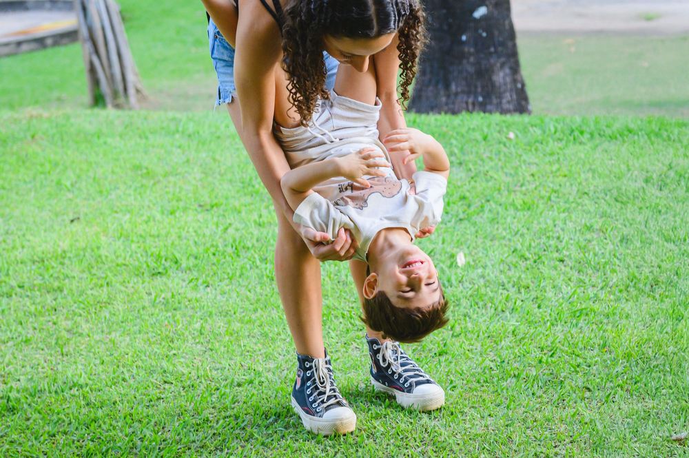 Playful moment on green grass as someone holds a child upside down during outdoor playtime at the park.