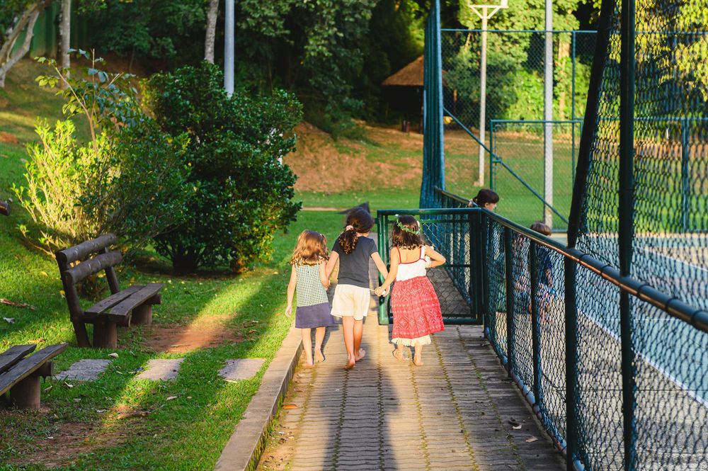 People walking along a sunlit path with decorative metal railings through lush green park surroundings.