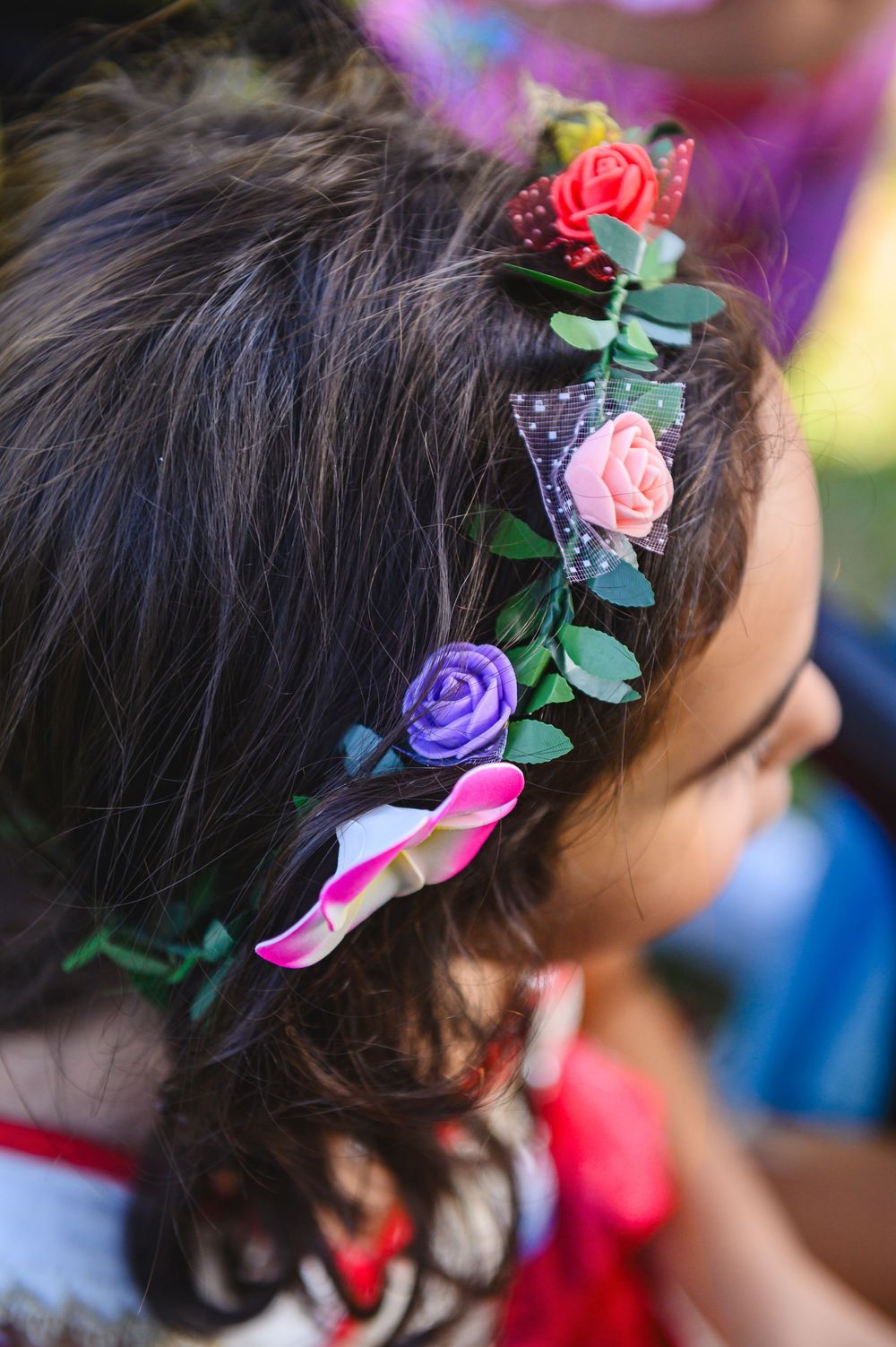 Delicate colorful floral headband with pink, purple and red roses adorning dark hair in soft focus.