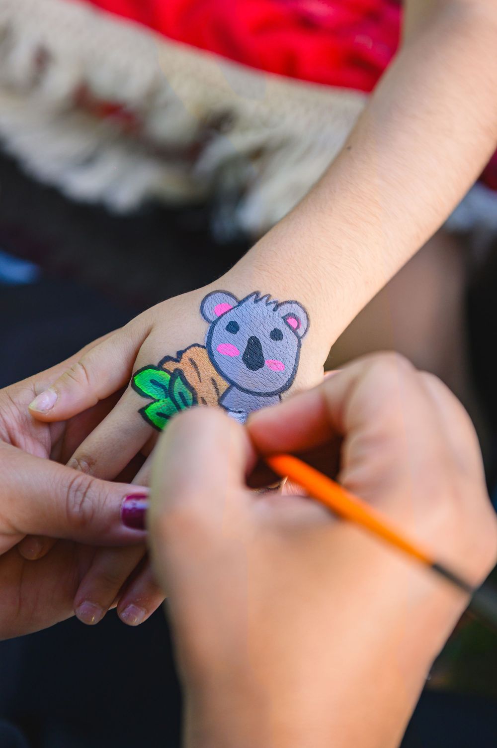 Someone drawing a cute purple koala design as face paint or temporary tattoo art with an orange marker.