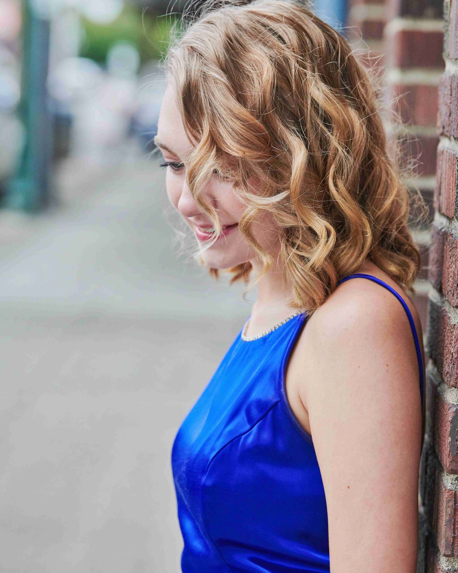 Beautiful high school senior female outside Liberty Theatre in Puyallup, leaning against brick wall, looking down.