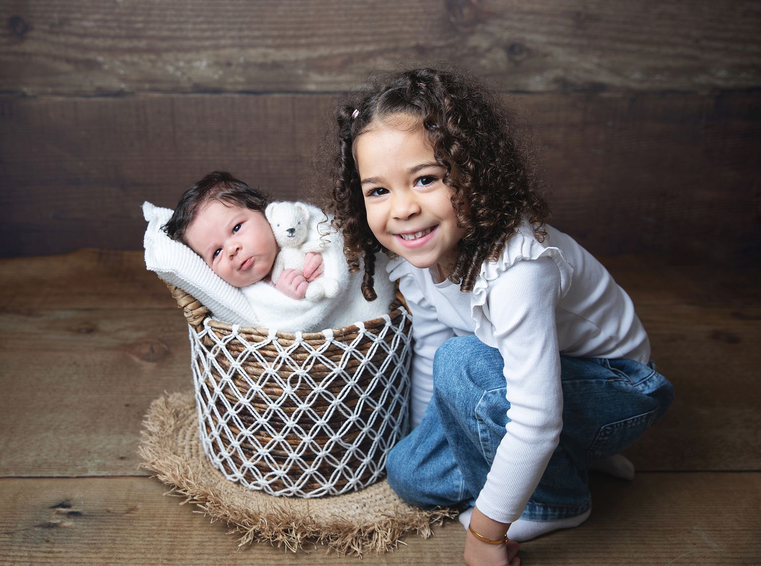 London newborn and sibling photography portraits showing sleeping infant in baskets with sibling poses on wooden floor.