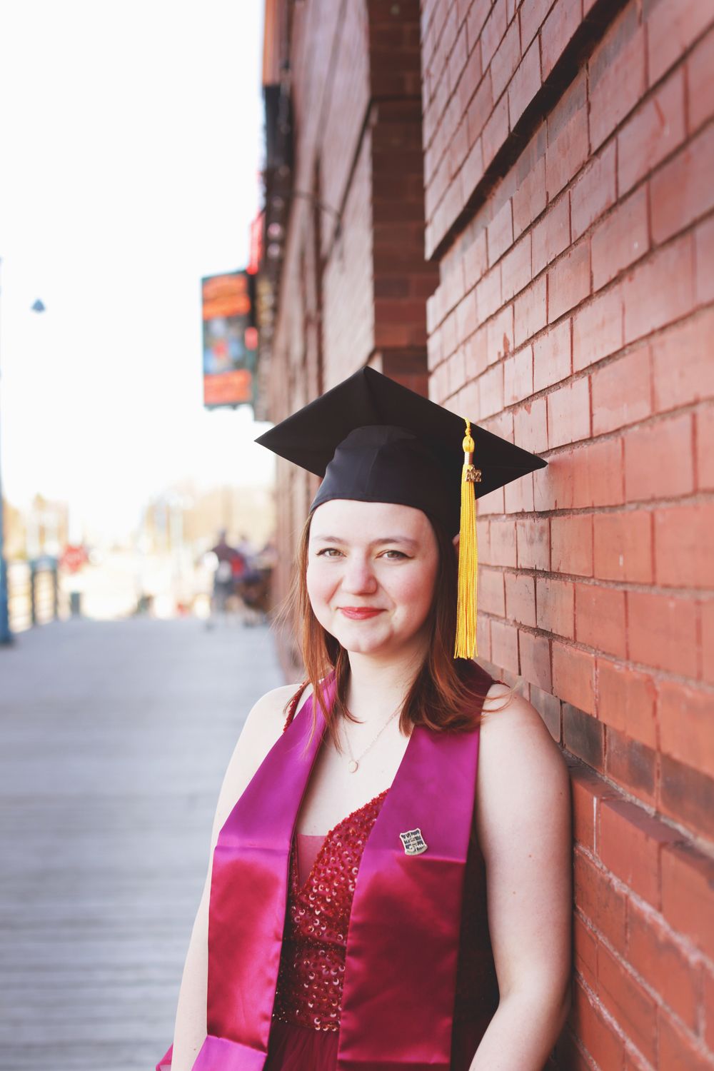 Graduation photos of someone wearing a burgundy sash and black cap against a brick wall background.