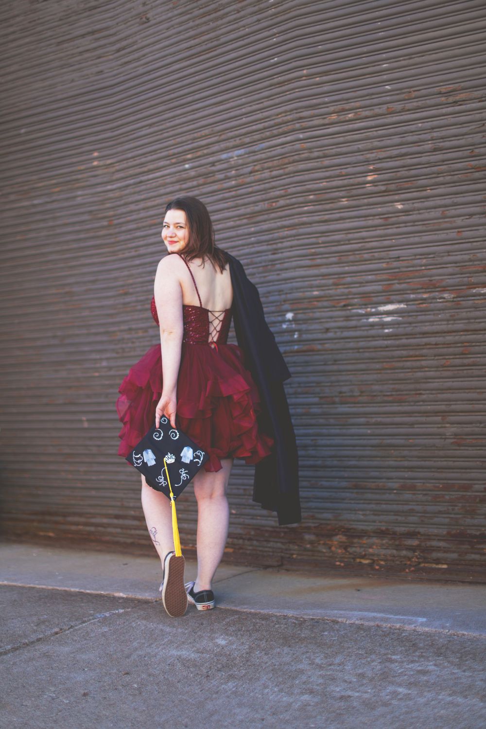 A person in a red dress crouches low against a corrugated metal wall in an urban setting.