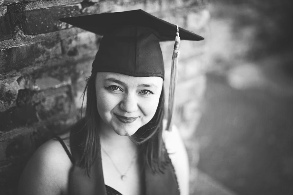 A black and white graduation photo collage showing various poses of a graduate in cap and gown against a brick wall.