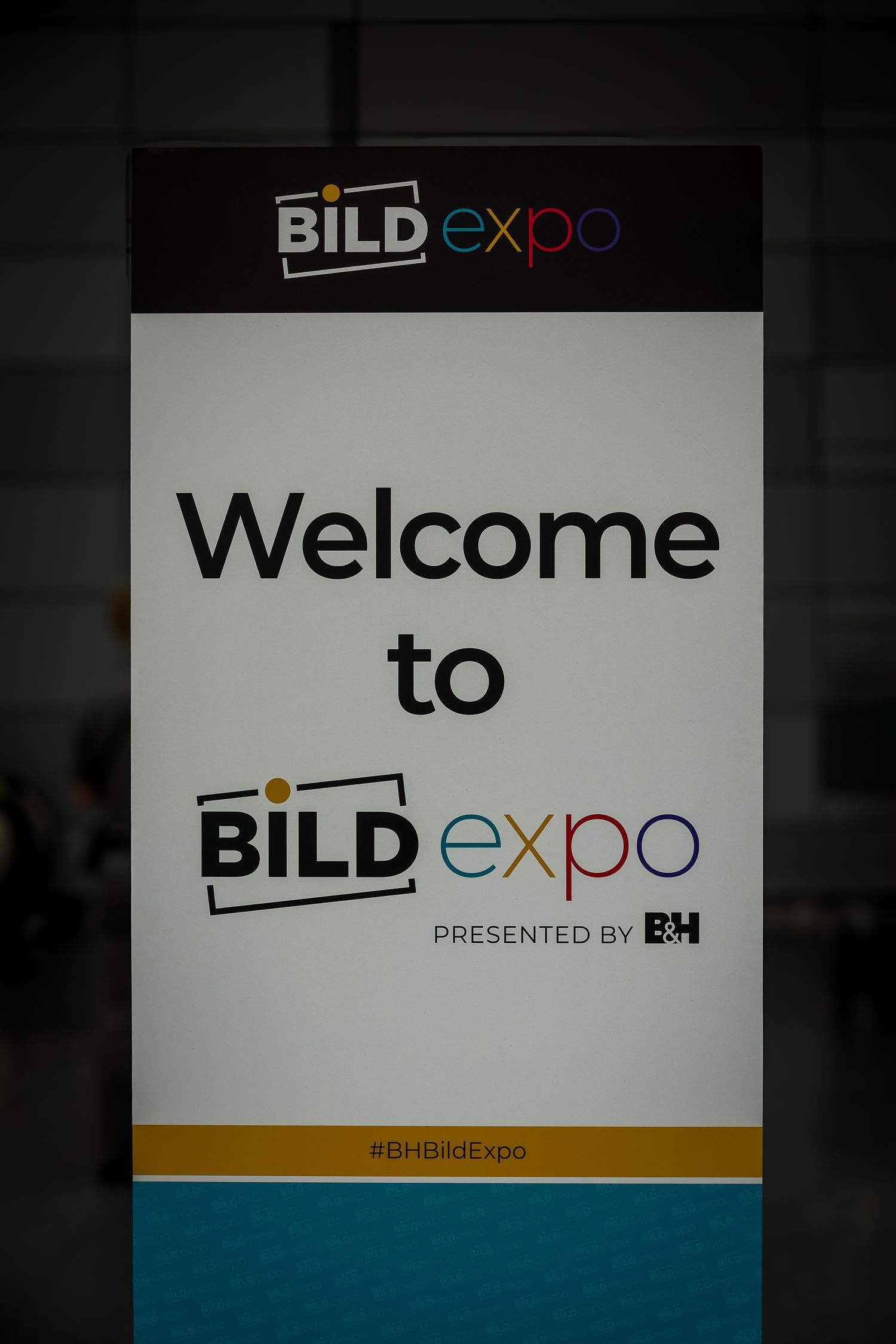A vertical welcome sign displaying 'Welcome to BILD expo' with company branding in black and teal colors.