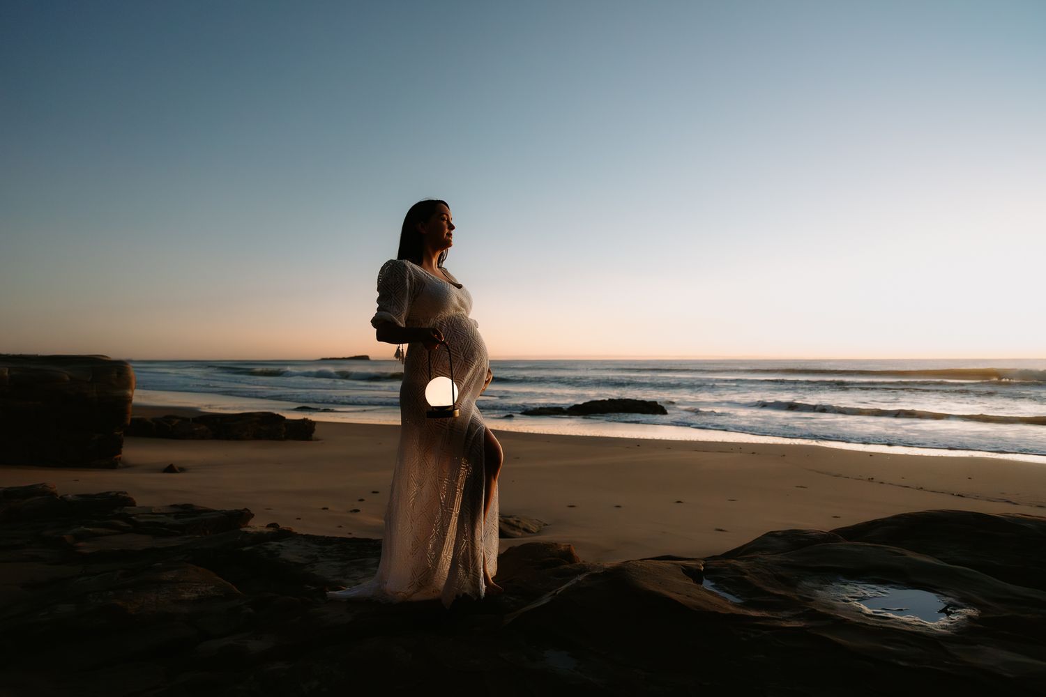 Silhouette of expectant mother standing on beach at sunset.