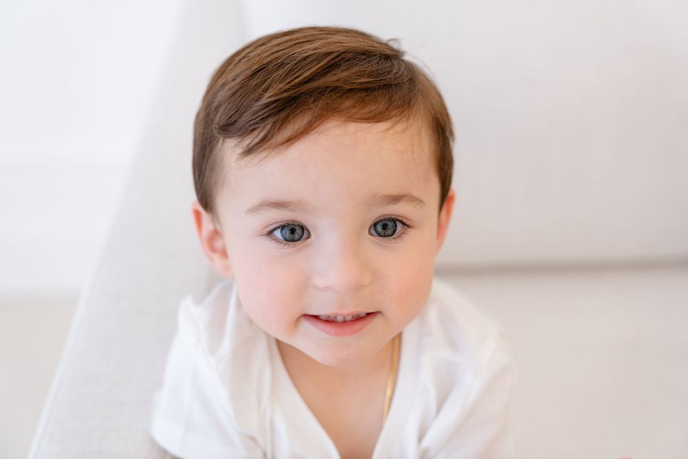 A smiling toddler in a white shirt poses against a bright white background.