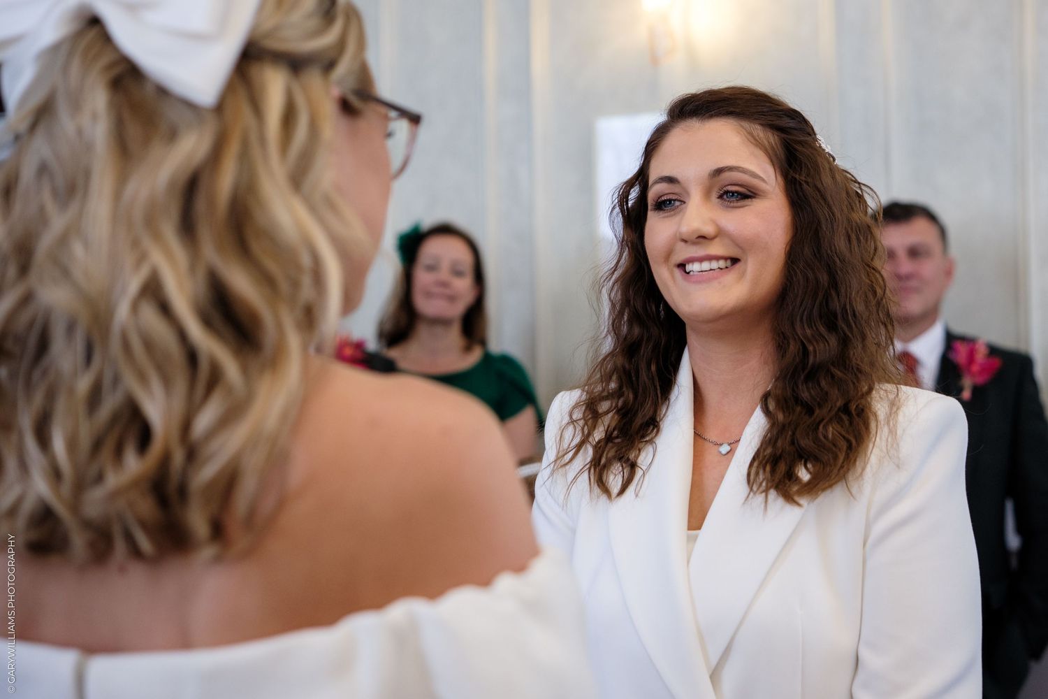 Two people share a joyful moment during a wedding ceremony with guests looking on in the background.