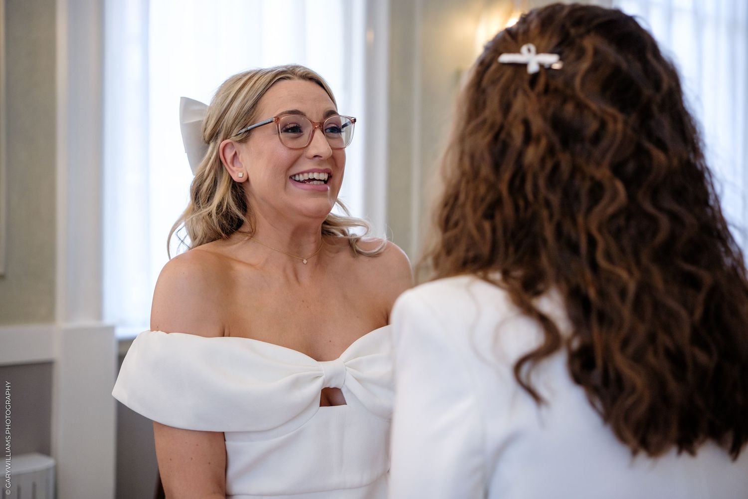Two people in white smiling in conversation during a special occasion.