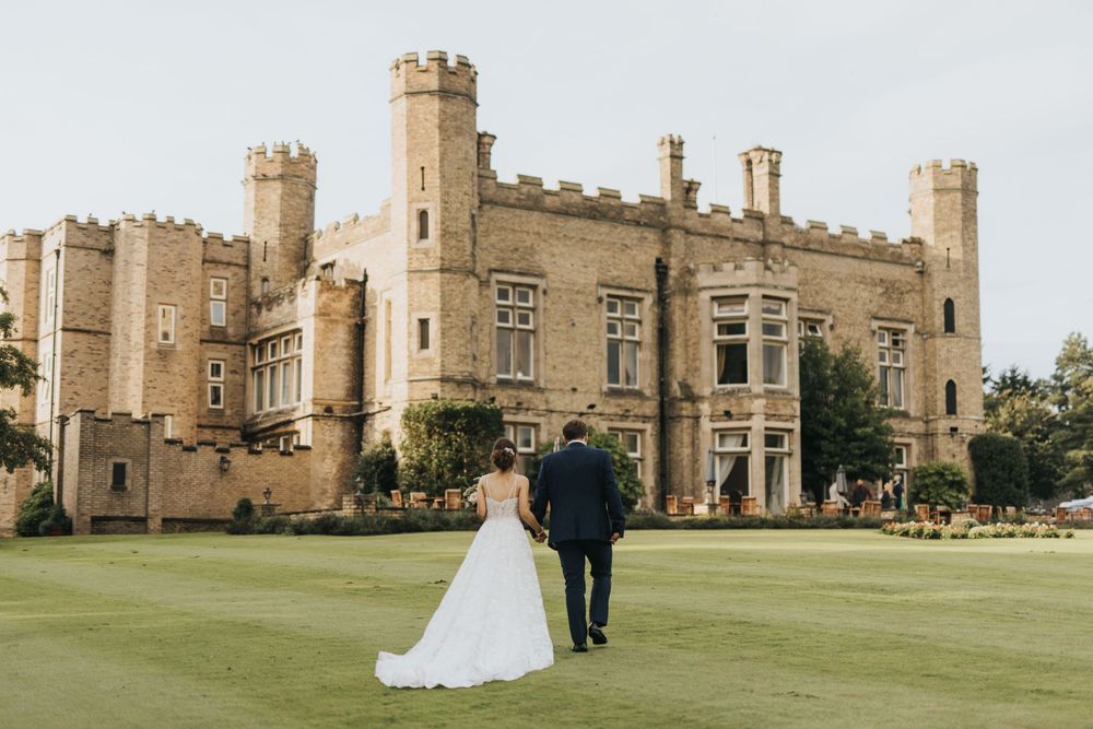 Wedding couple walk across a manicured lawn towards Cave Castle - taken by Grimsby photographer.