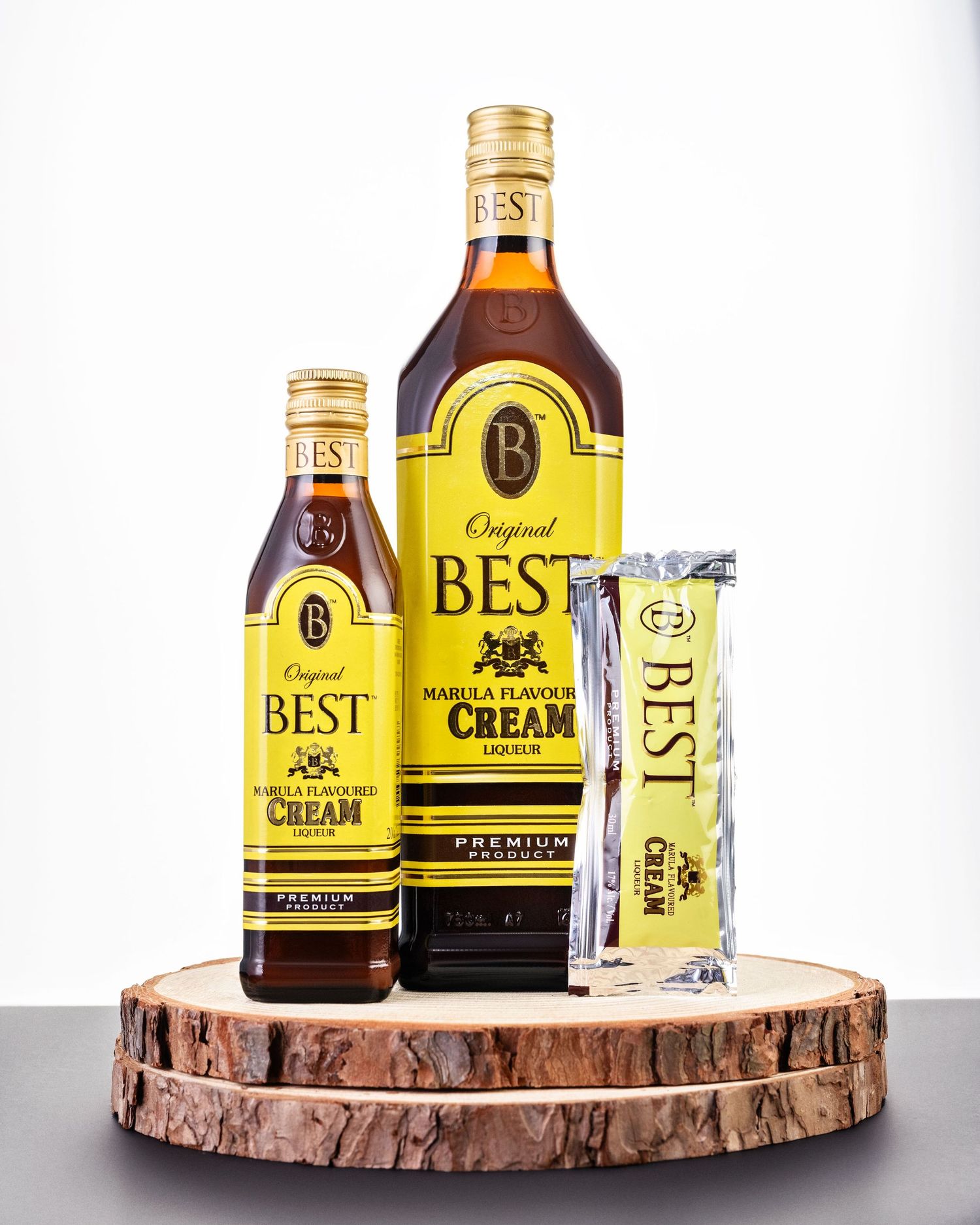 Three Best Cream Liquor products displayed on a rustic wood slice including a bottle, mini bottle, and snack bar.
