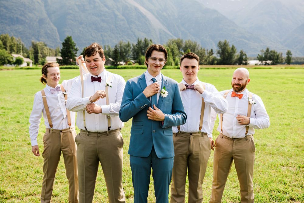 Groomsmen in casual attire with suspenders and bowties pose outdoors.