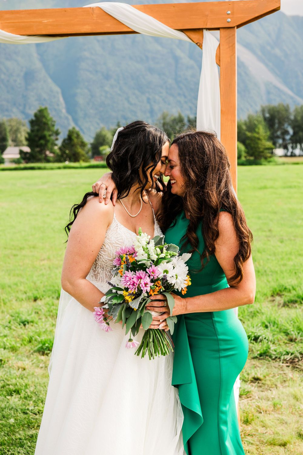 Two people share an intimate moment under wooden arch with bouquet and mountain backdrop.