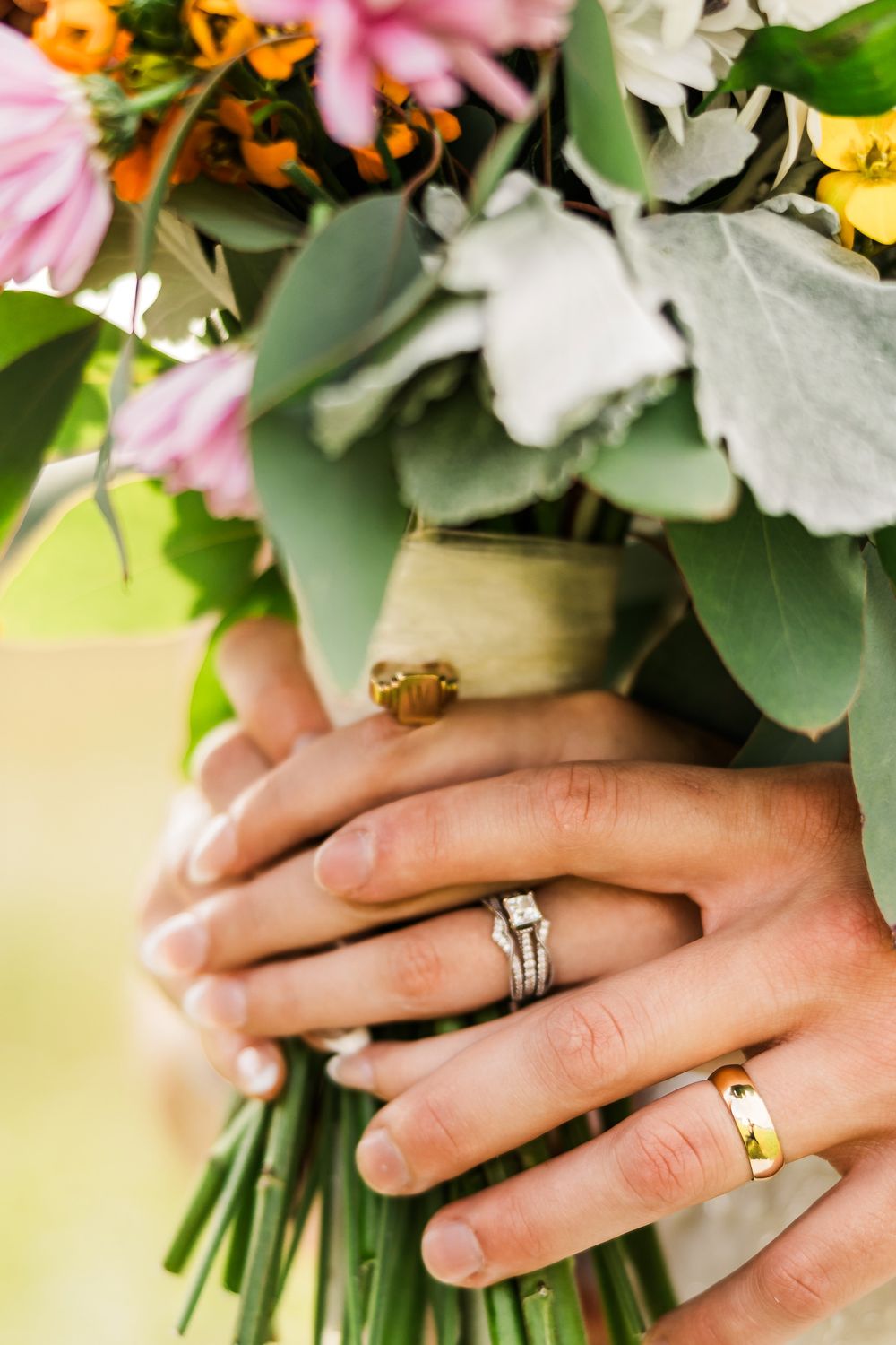Wedding rings displayed on hands holding vibrant floral bouquet.